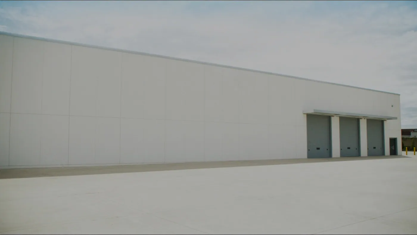 A white precast wall of an industrial plant with three closed grey dock doors and an empty concrete apron