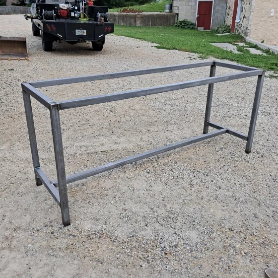 A welded rectangular steel table frame standing on a gravel drive