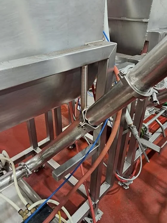 Stainless steel process piping and a hopper on a red painted plant floor