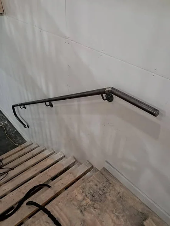 A steel handrail mounted on a white wall above a stair under construction